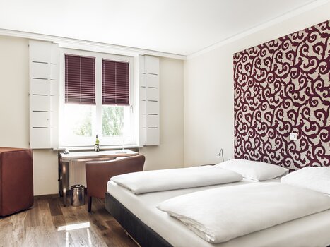 A bright hotel room with two beds, a desk, and window. | © Weitzer