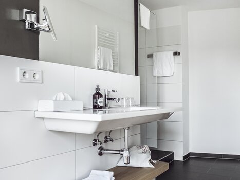 A modern bathroom featuring a sink and wooden shelf. | © Das Weitzer