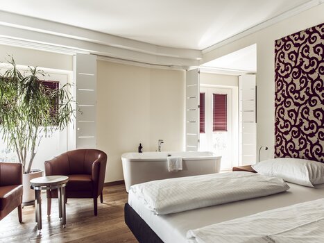 A bedroom featuring a bed, bathtub, and seating area. | © Das Weitzer