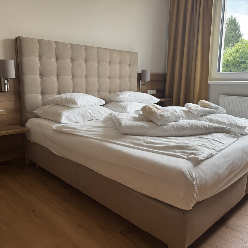 Heller Raum mit Doppelbett, Kissen und Tagesdecke. | © Der Marienhof