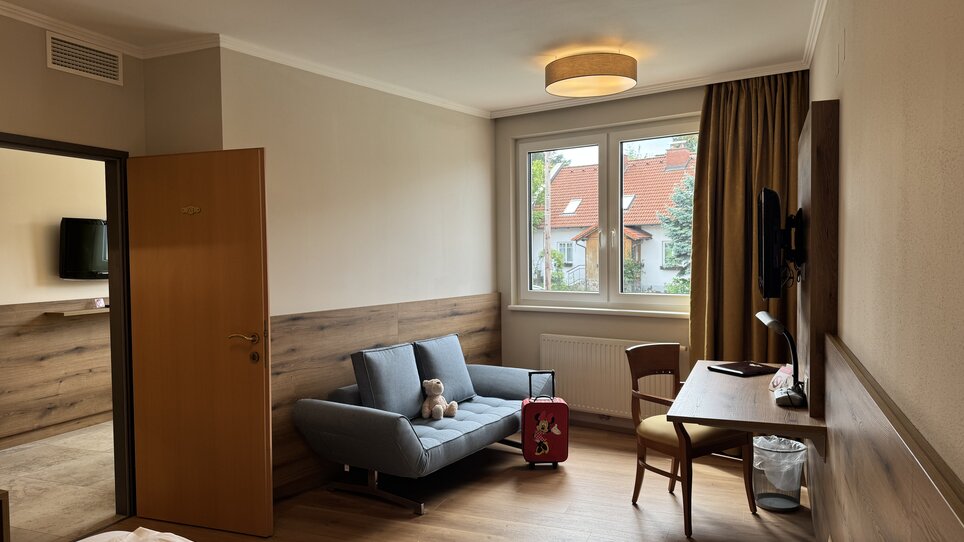 Spacious hotel room featuring a sofa, desk, and TV. | © Der Marienhof