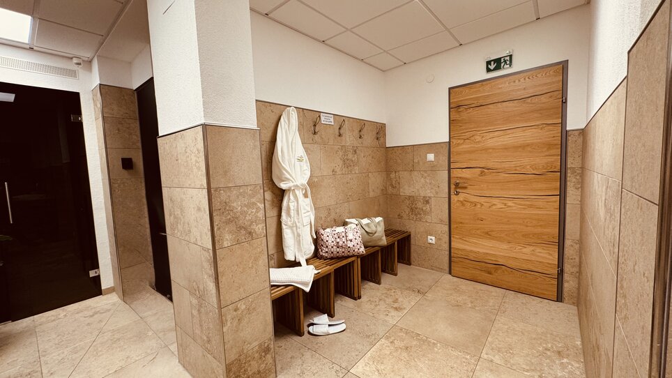 A modern changing area with wooden benches, bathrobes, and a wooden door. | © Der Marienhof