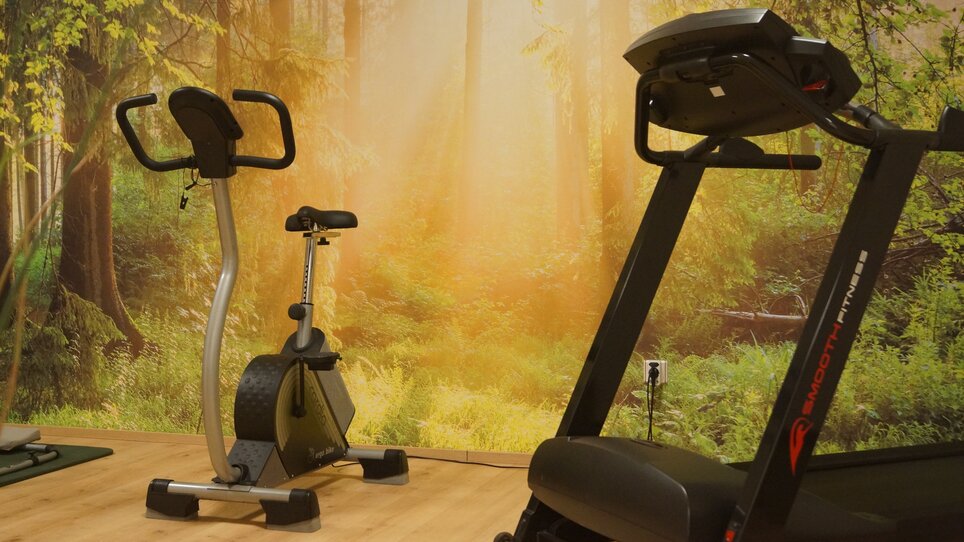 Two pieces of cardio equipment in a room with forest wallpaper. | © Der Marienhof