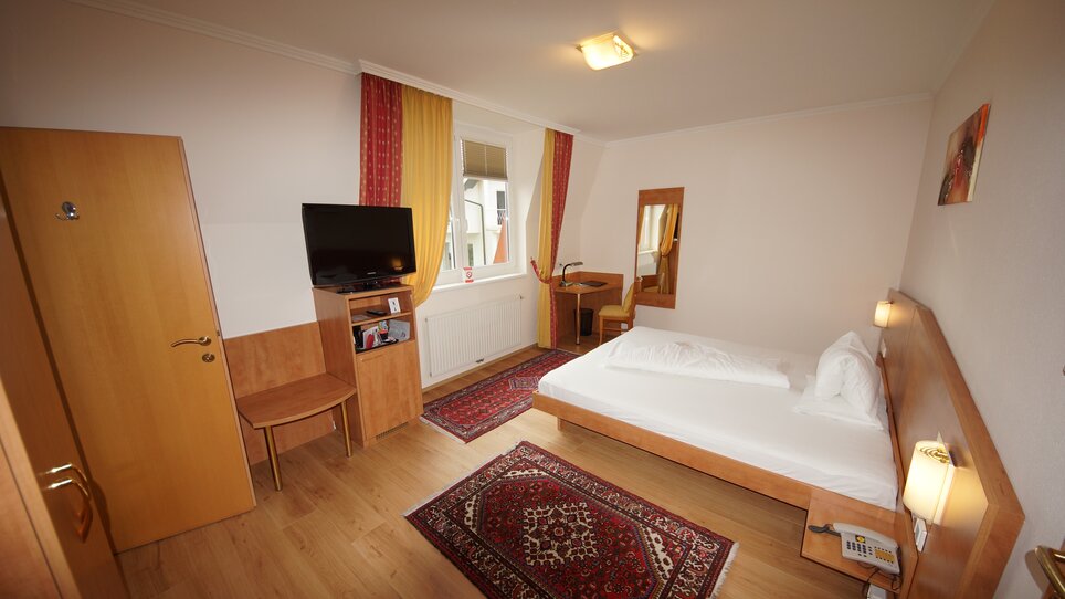 Bright hotel room featuring double bed, TV, and desk. | © Der Marienhof