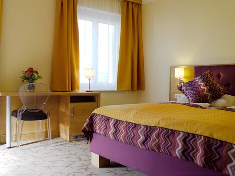 Bright bedroom with wooden details and purple accents. | © Hotel Drei Raben
