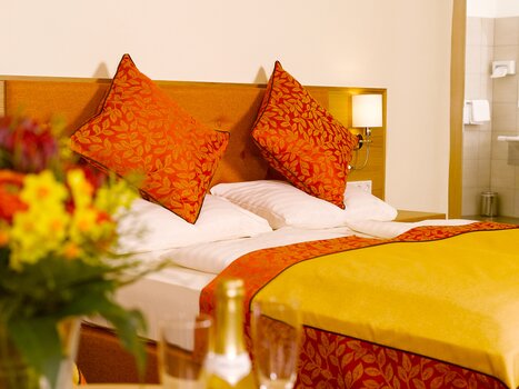A cozy bedroom with orange pillows and flowers. | © Hotel Drei Raben