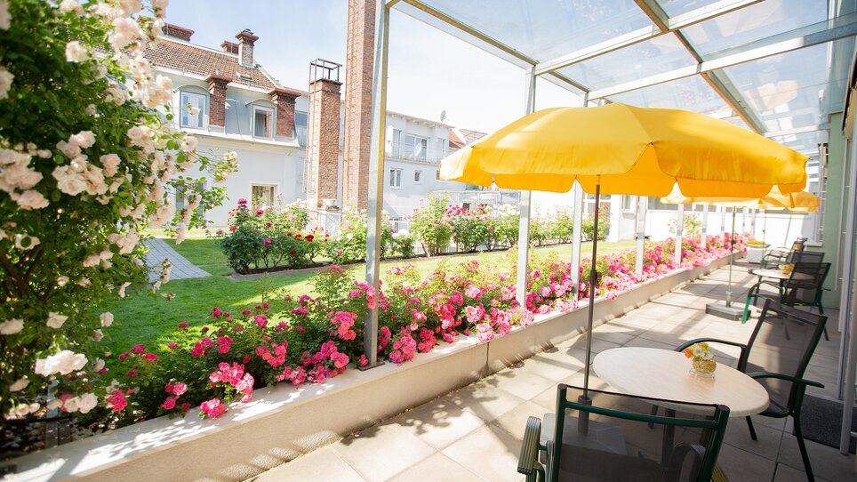 Terrasse mit gelben Schirmen und Rosenbeeten. | © Gollner