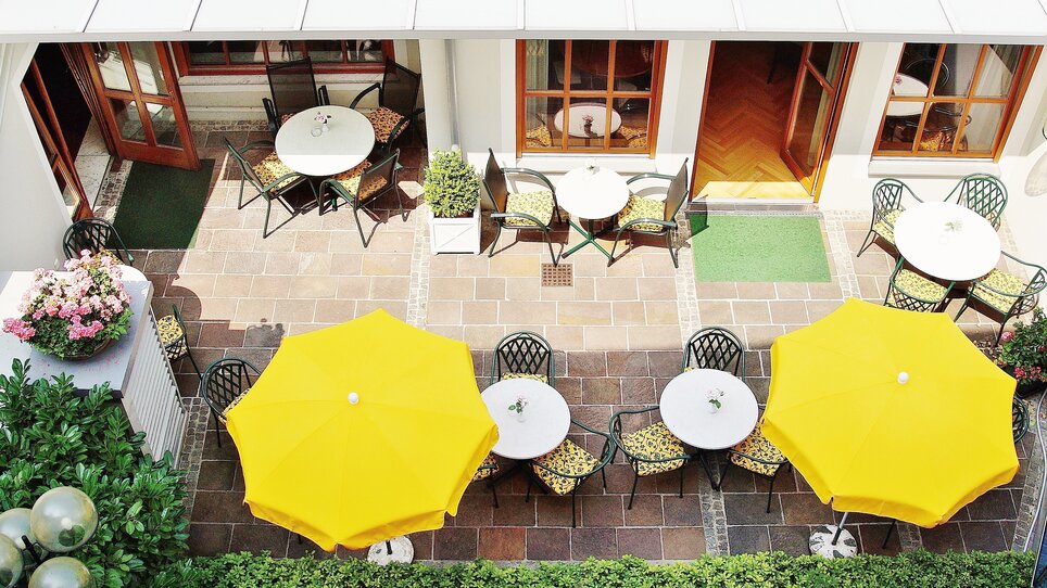 Überblick über eine Terrasse mit Tischen, Stühlen und gelben Sonnenschirmen. | © Gollner