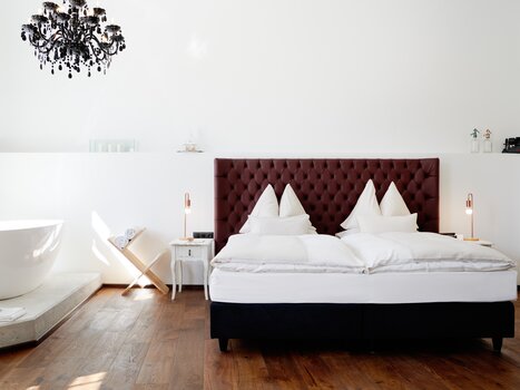 Una camera da letto con letto matrimoniale, una vasca da bagno indipendente e un lampadario. | © Weitzer Hotels