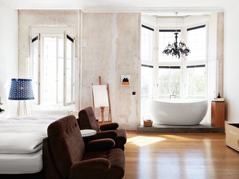 Camera luminosa con finestra grande, vasca da bagno indipendente, due sedie e televisore. | © Weitzer Hotels