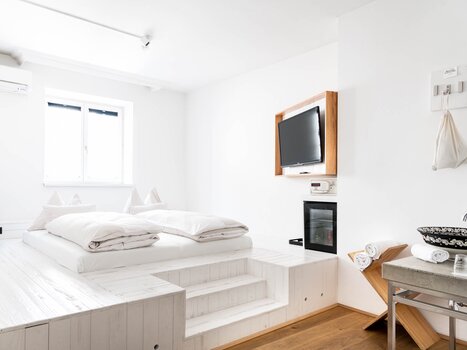 Una camera da letto minimalista con un letto rialzato e TV.