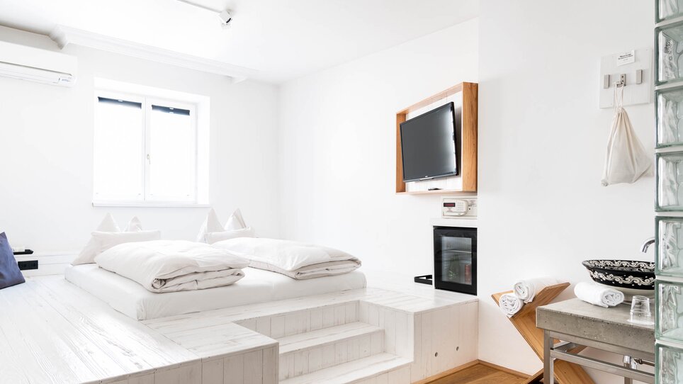 Ein minimalistisches Schlafzimmer mit einem erhöhten Bett und Fernseher.