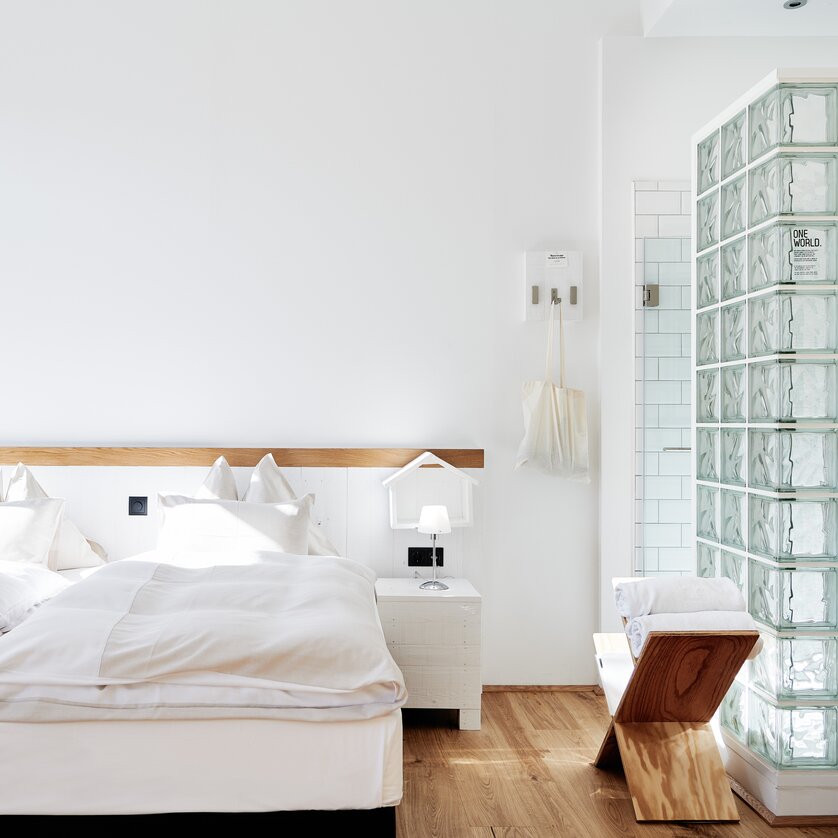 Camera con letto matrimoniale, doccia in vetro e dettagli in legno.