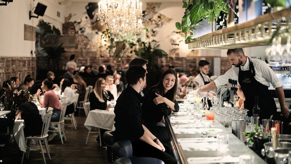 Belebtes Restaurant mit Gästen, der Barkeeper serviert Drinks.