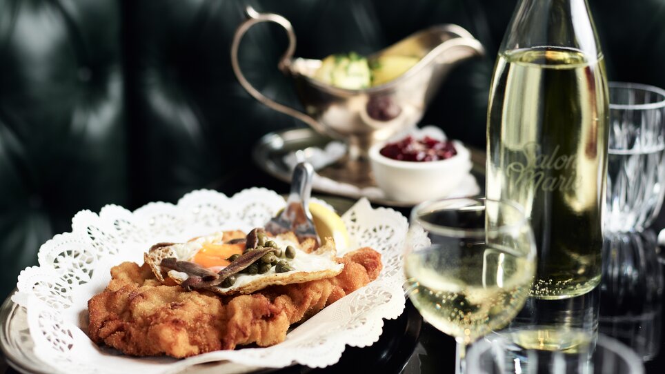 Ein Teller mit paniertem Schnitzel, Sekt und Beilagen auf einem Tisch.