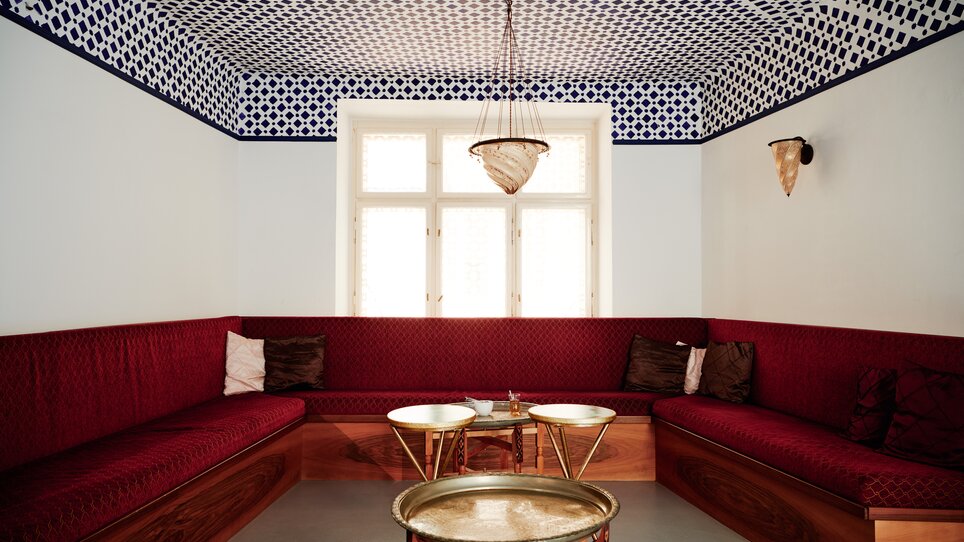 Stilvolles marokkanisches Zimmer mit roten Bänken und dekorativem Muster an der Decke.