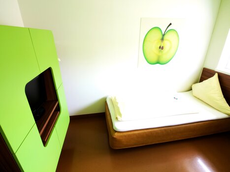Una stanza con un armadio verde, un letto e un'immagine di una mela sul muro. | © Hotel Greenrooms