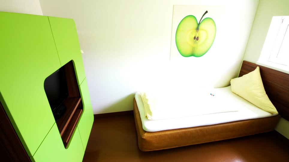 Una stanza con un armadio verde, un letto e un'immagine di una mela sul muro. | © Hotel Greenrooms