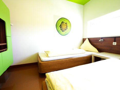 Una stanza con due letti, design verde e arte a parete con kiwi. | © Hotel Greenrooms