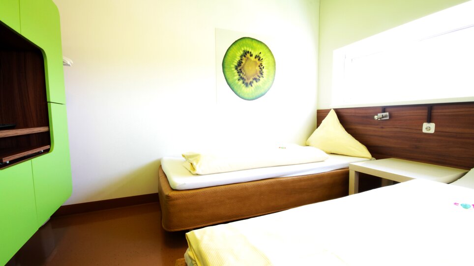 Una stanza con due letti, design verde e arte a parete con kiwi. | © Hotel Greenrooms