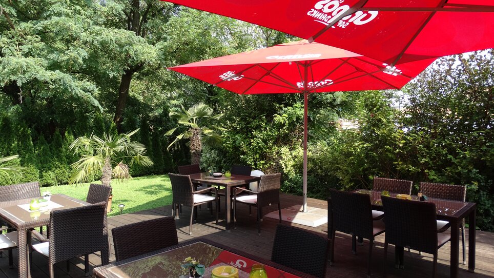 Tavoli e sedie sotto ombrelli rossi in un giardino.