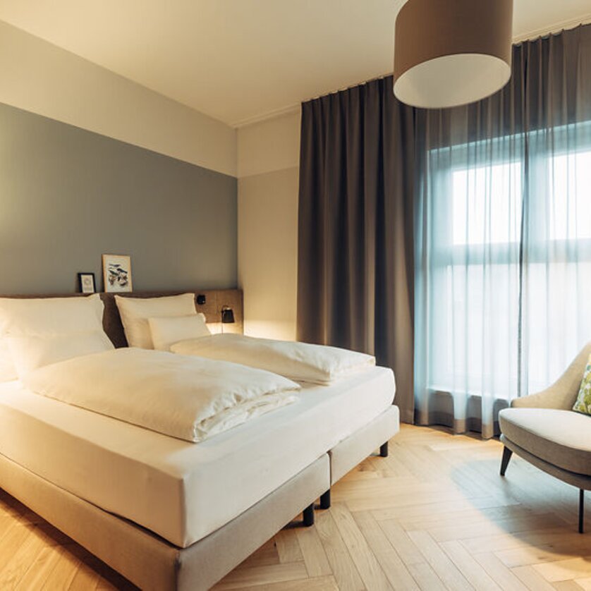 Camera luminosa con due letti e una poltrona in harry's home Graz-Smart City. | © harry's home Graz-Smart City - Daniel Zangerl