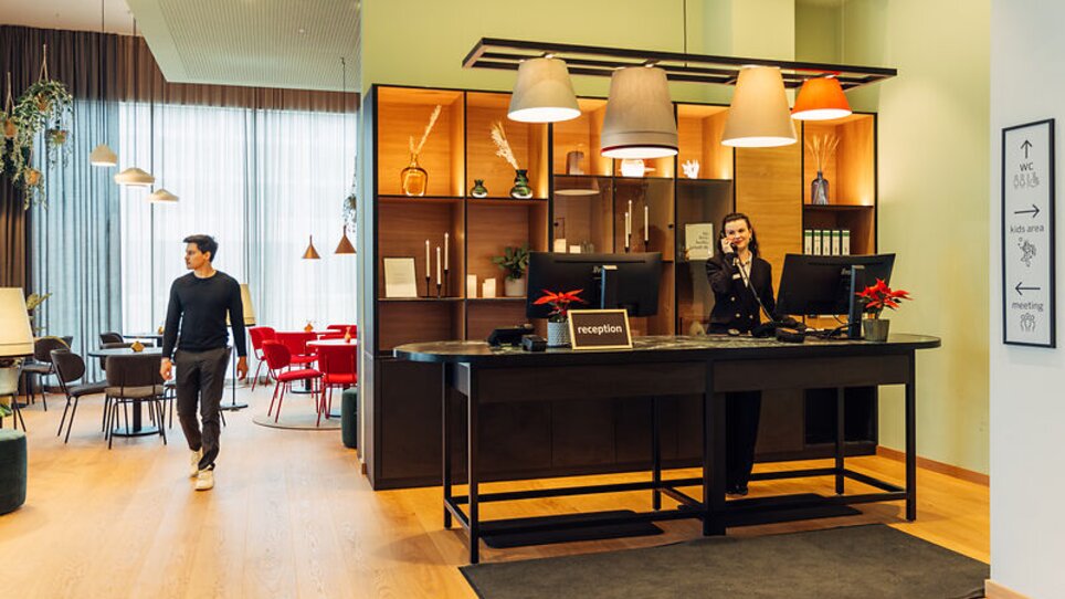 Un'area reception luminosa con un membro dello staff al telefono nell'harry's home Graz-Smart City. | © harry's home Graz-Smart City - Daniel Zangerl