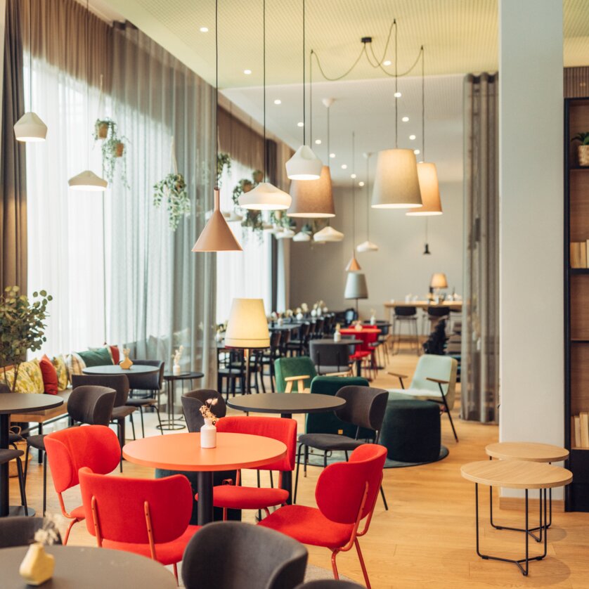 Hell erleuchtet Café mit bunten Stühlen und Pflanzen im harry's home Graz-Smart City. | © harry's home Graz-Smart City - Daniel Zangerl