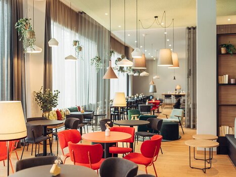 Caffè illuminato con sedie colorate e piante al'harry's home Graz-Smart City. | © harry's home Graz-Smart City - Daniel Zangerl