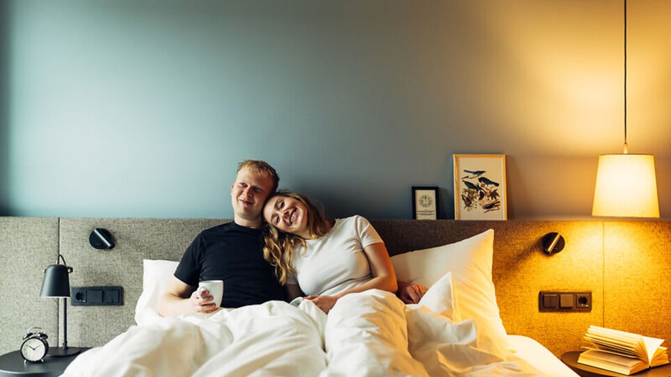Liebespaar entspannend im Bett mit einer Tasse Kaffee im harry's home Graz-Smart City. | © harry's home Graz-Smart City - Daniel Zangerl