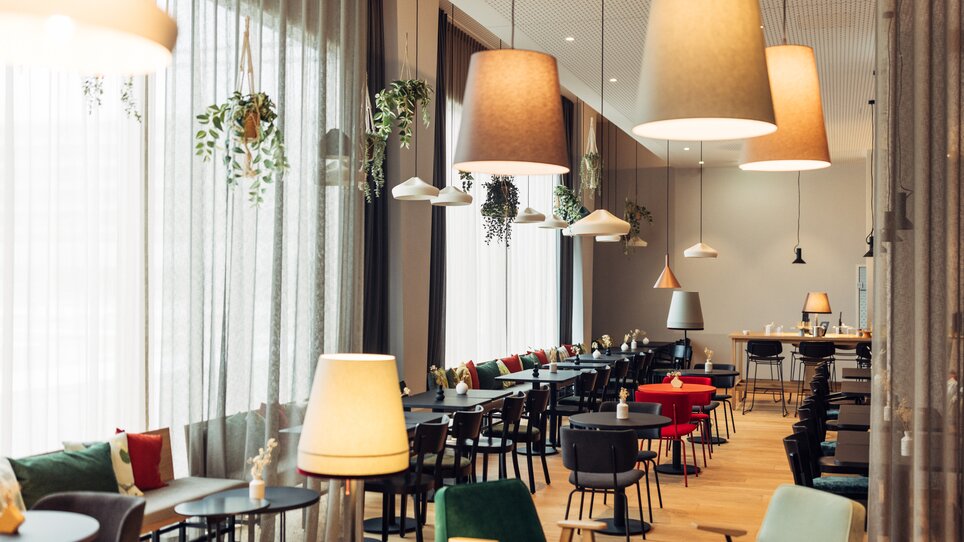 Innenansicht eines Cafés mit Tischen, Stühlen und Beleuchtung. | © harry’s home hotels - Daniel Zangerl