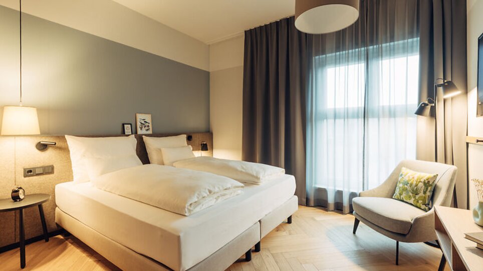 Camera d'hotel accogliente con letto matrimoniale e una poltrona per leggere. | © Harrys Home Graz Smart City - Daniel Zangerl