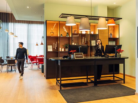 A receptionist at the desk as a guest walks by. | © Harrys Home Graz Smart City - Daniel Zangerl