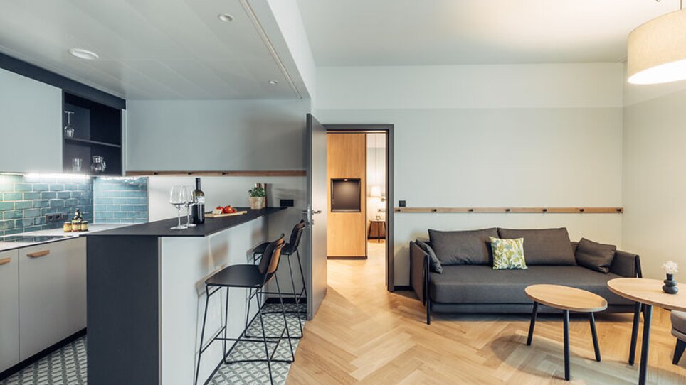 Cucina aperta e zona soggiorno con posti a sedere e accesso a una camera da letto. | © Harrys Home Graz Smart City - Daniel Zangerl