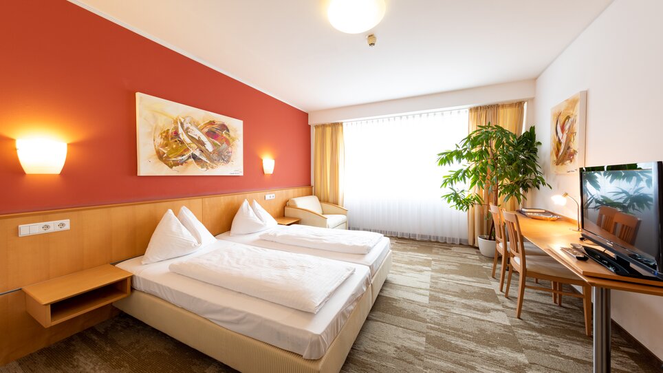 Modern room with two beds, TV, and plants. | © Harry Schiffer