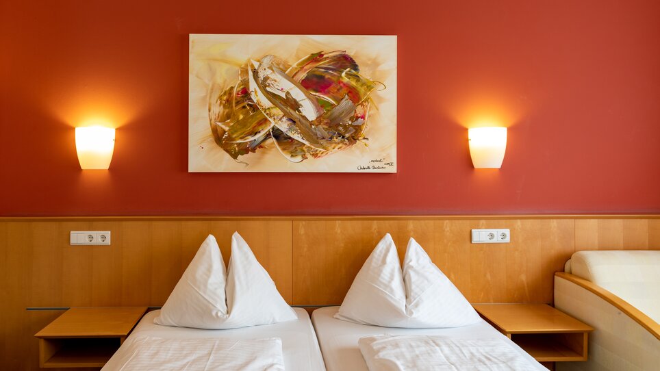 A bright room with two beds, red wall, and modern art. | © Harry Schiffer