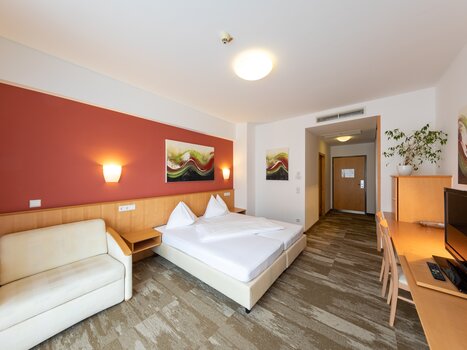 Luminoso camera d'hotel con letto matrimoniale, divano e scrivania. | © Harry Schiffer