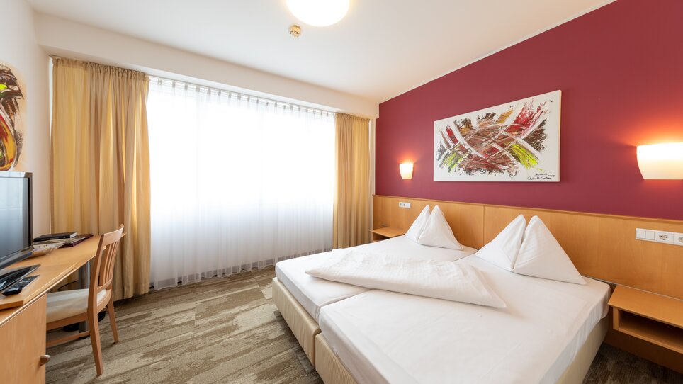 Brightly decorated room with double bed and TV. | © Harry Schiffer