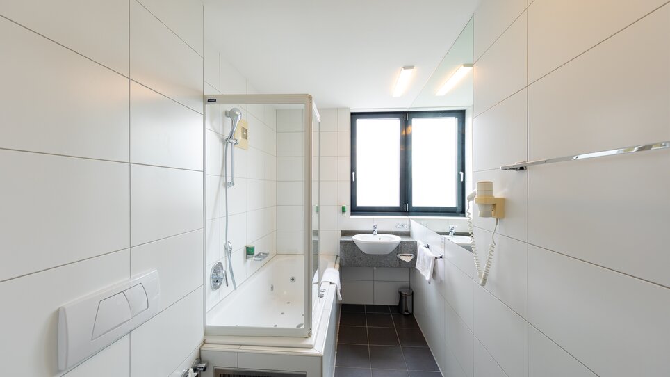 Bright bathroom with shower, sink, and window. | © Harry Schiffer