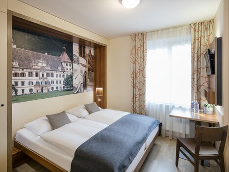 Camera d'albergo moderna con letto matrimoniale, scrivania e finestra. | © JUFA Hotel Graz City