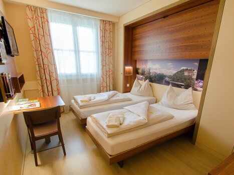 Camera d'hotel accogliente con due letti singoli e una scrivania. | © JUFA Hotel Graz City