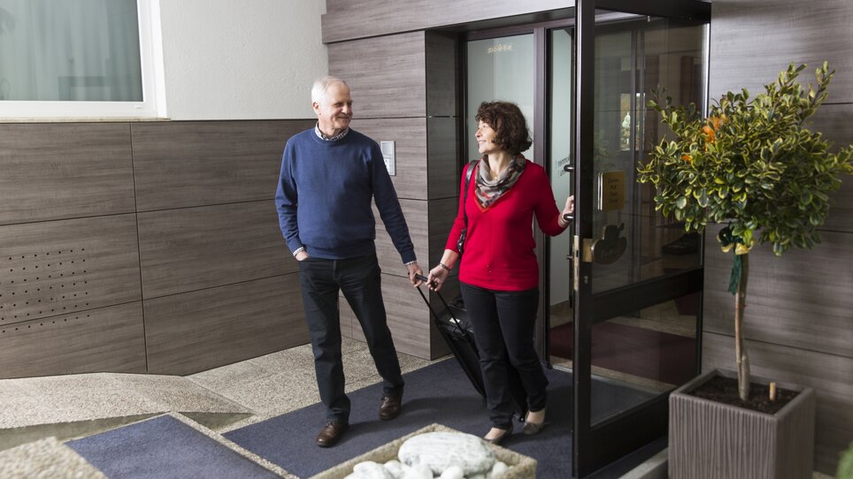 Ein Paar verlässt das Hotel Kern Buam mit einem Rollkoffer. | © Hotel Kern Buam