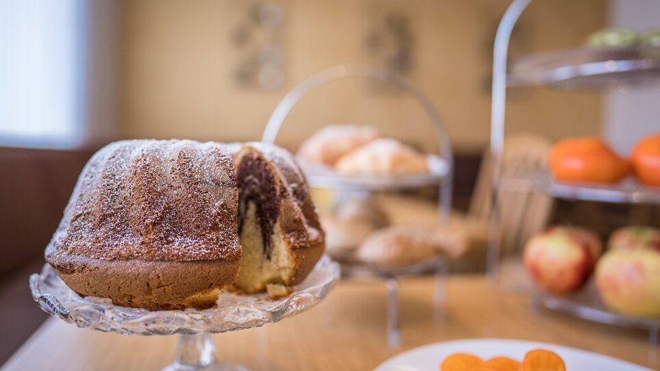 Ein dekorierter Kuchen auf einem Tisch mit Obst und Gebäck im Hintergrund. | © Mario Gimpl