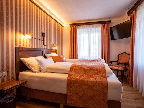 Una camera d'hotel con letto matrimoniale, accenti arancioni e TV. | © Lendplatzl GmbH