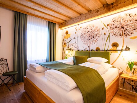 Una stanza luminosa con soffitto in legno, carta da parati floreale e un letto matrimoniale. | © Lendplatzl GmbH