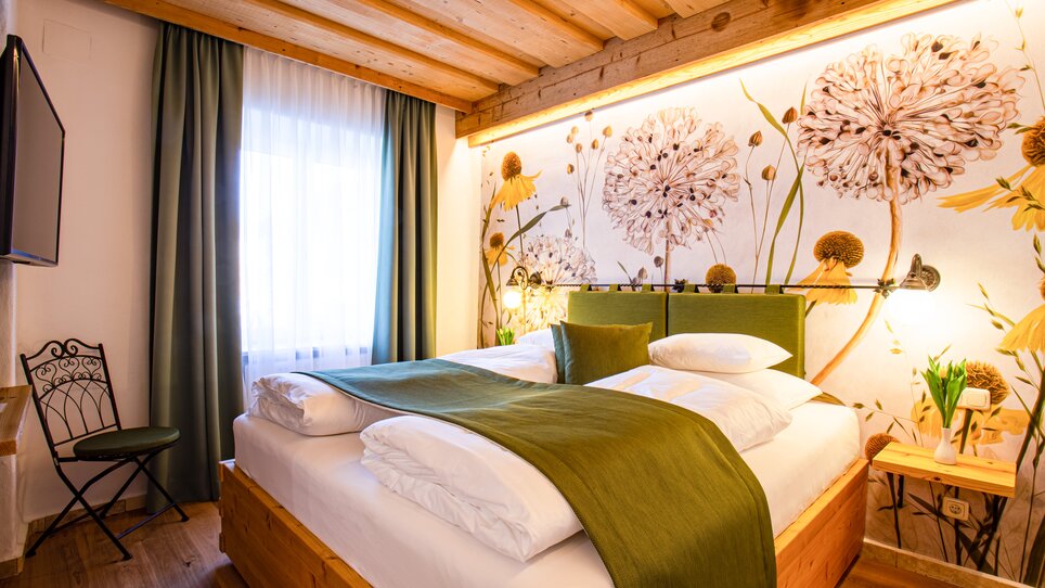 Ein helles Schlafzimmer mit Holzdecke, Blumenmuster an der Wand und einem Doppelbett. | © Lendplatzl GmbH