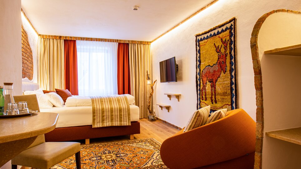 Doppelzimmer mit Teppich, TV und dekorativem Wandteppich. | © Lendplatzl GmbH