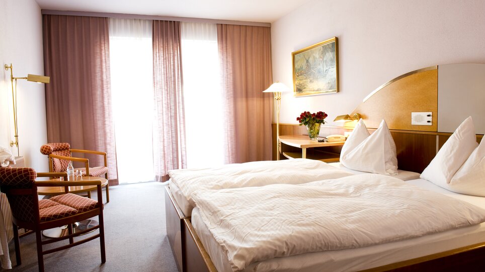 A bright room featuring a double bed with two pillows and cozy chairs. | © Lindenwirt