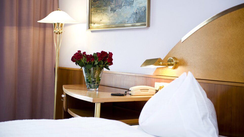 A double room with flowers, lamp, and telephone on the nightstand. | © Lindenwirt