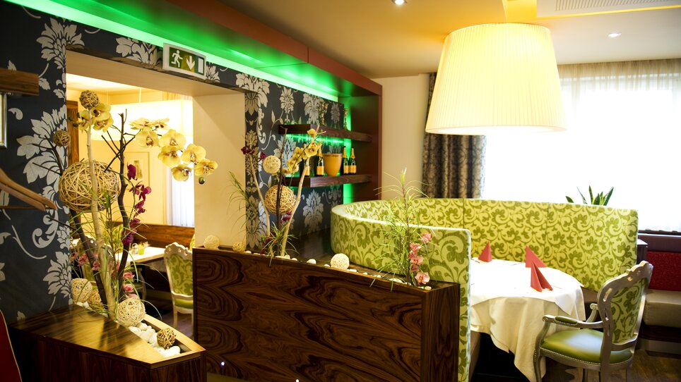 Elegant dining area with green couch, floral arrangement, and soft lighting. | © Lindenwirt